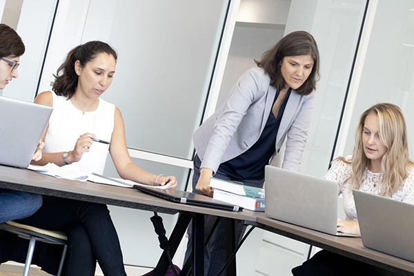 Three students at a table with laptops consult with their female mentor.